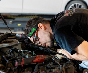 Mechanic inspecting a car engine in a garage, wearing a headlamp.