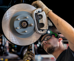 Mechanic working on a car's brake system. Wearing glasses and headlamp, he adjusts the caliper near a brake disc.
