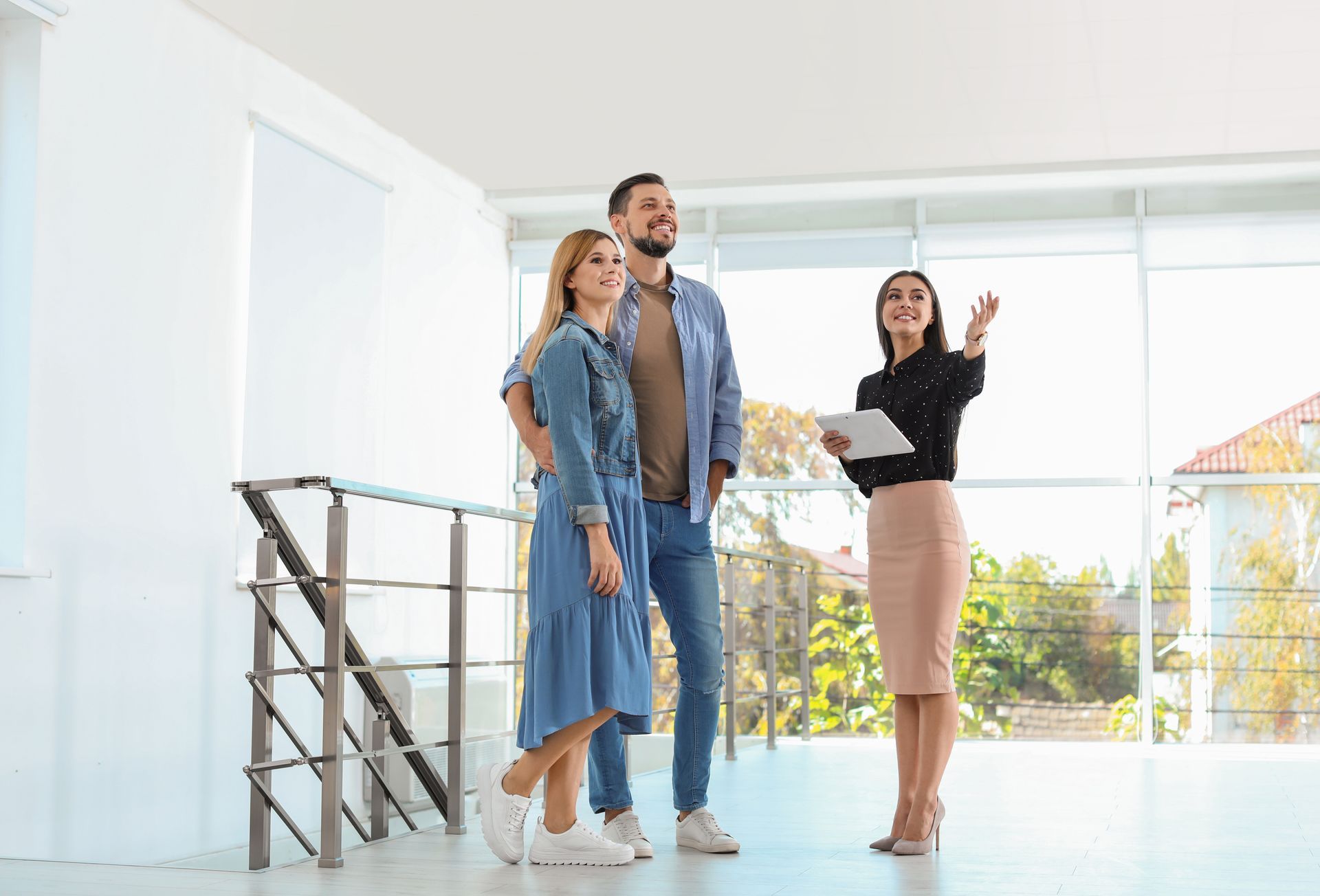 Real estate agent showing a couple a bright, empty room with large windows.
