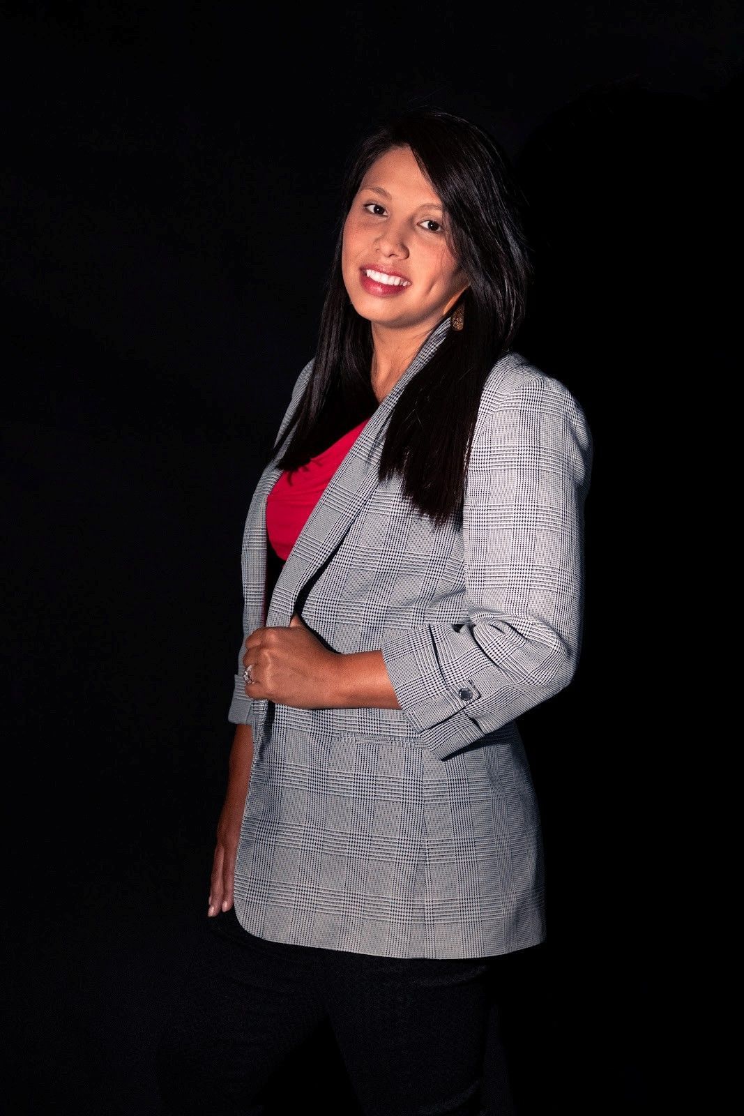 Woman in black suit holding paperwork, smiling in front of a white building with large windows.