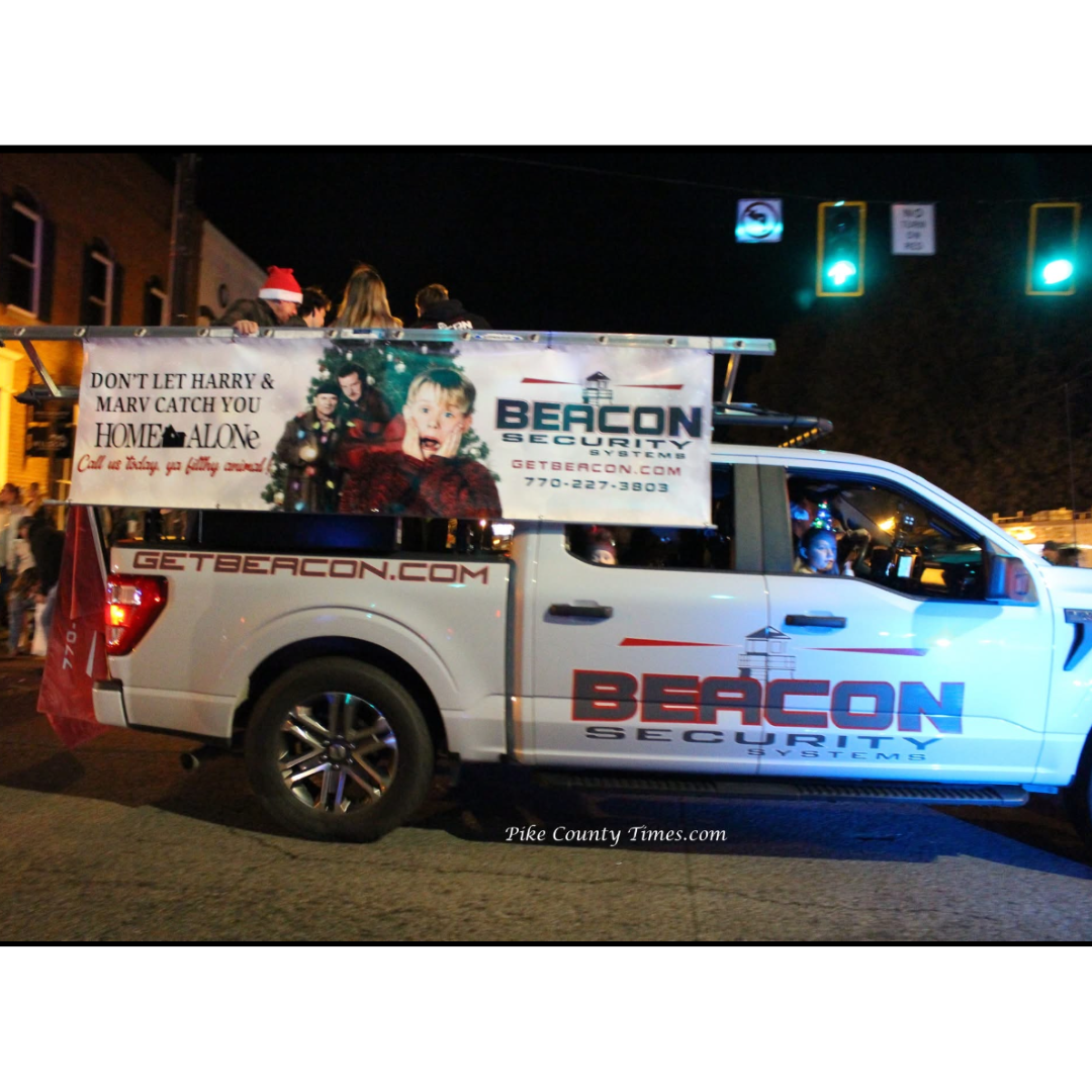 White BEACON pickup truck with campaign signage parked at night on a city street.