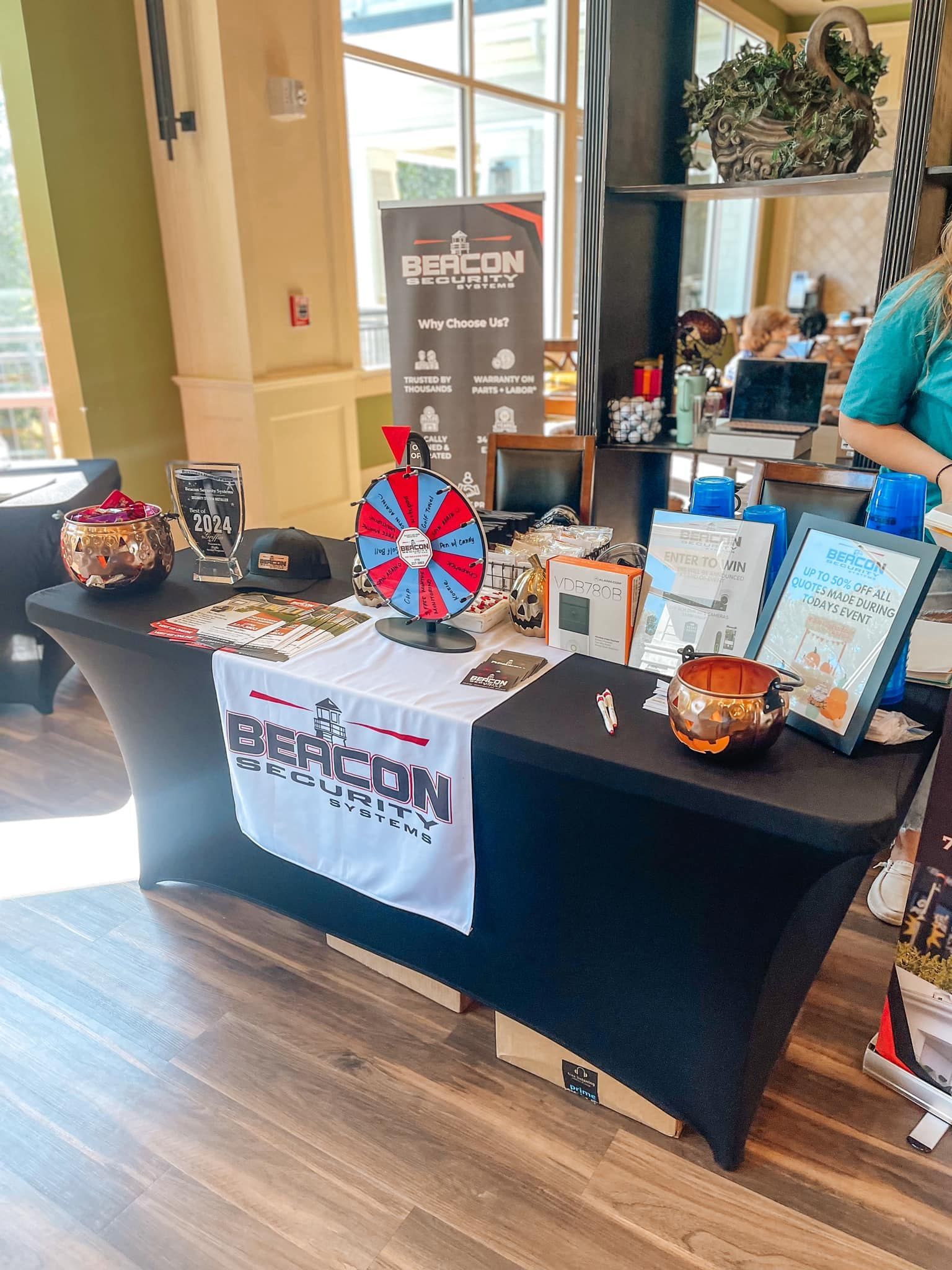 Auction display table with raffle wheel, gift baskets, and framed items in a lobby.