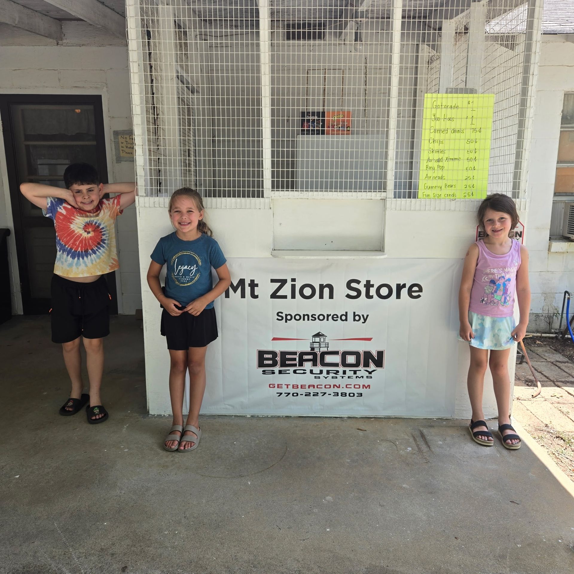 Three children standing outside a building beside a sign that reads “Zion Store” and “Beacon.”