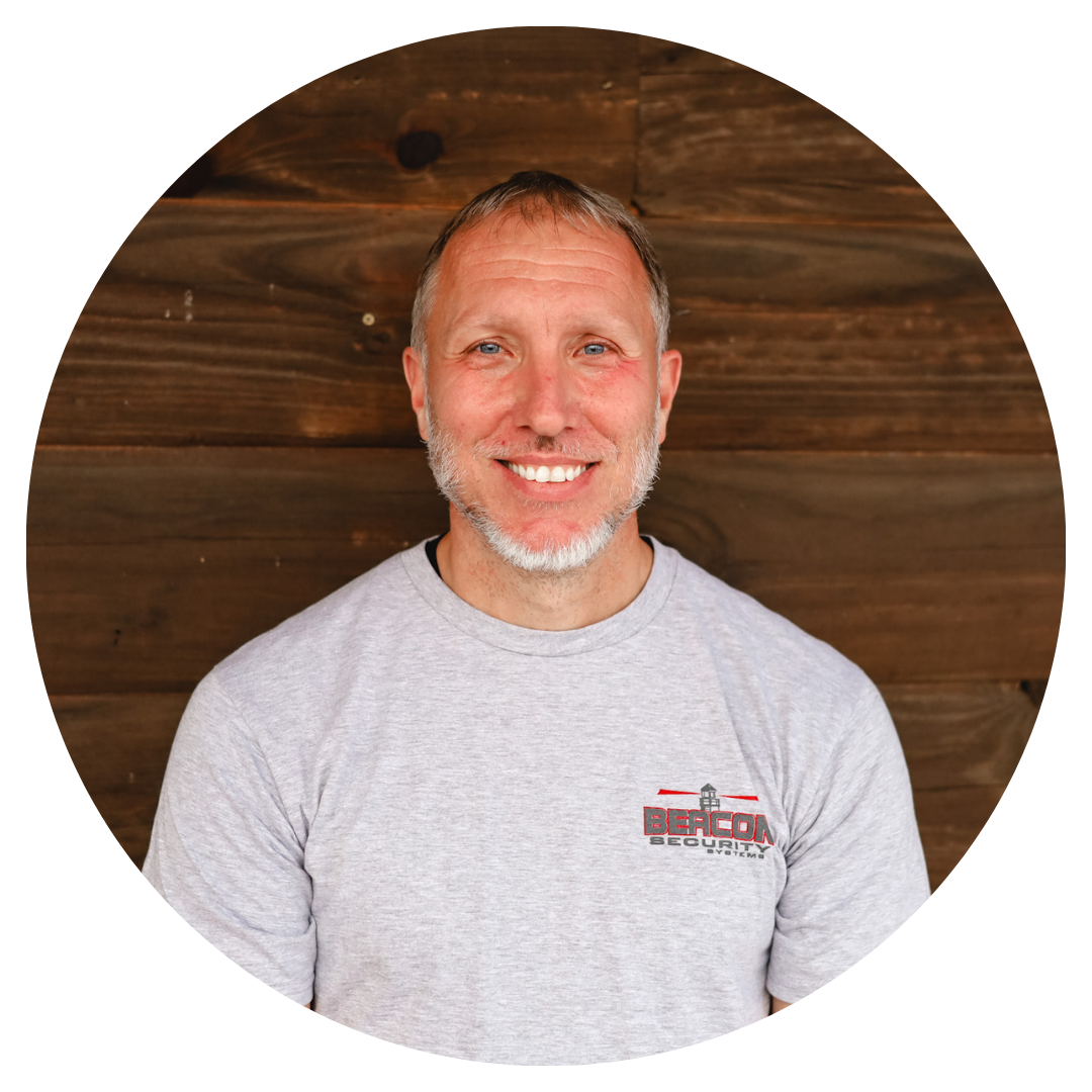 A man with a beard is smiling in front of a wooden wall.