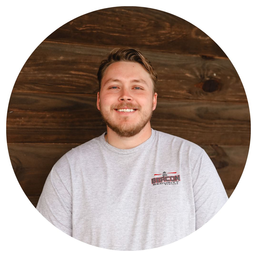 A man with a beard is smiling in front of a wooden wall.