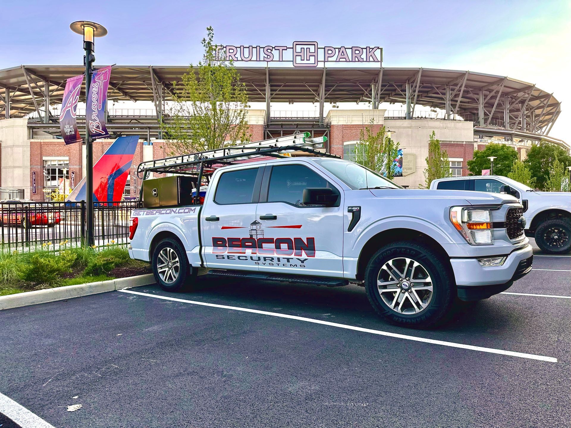 White pickup truck parked outside a stadium with a rainbow in the sky.