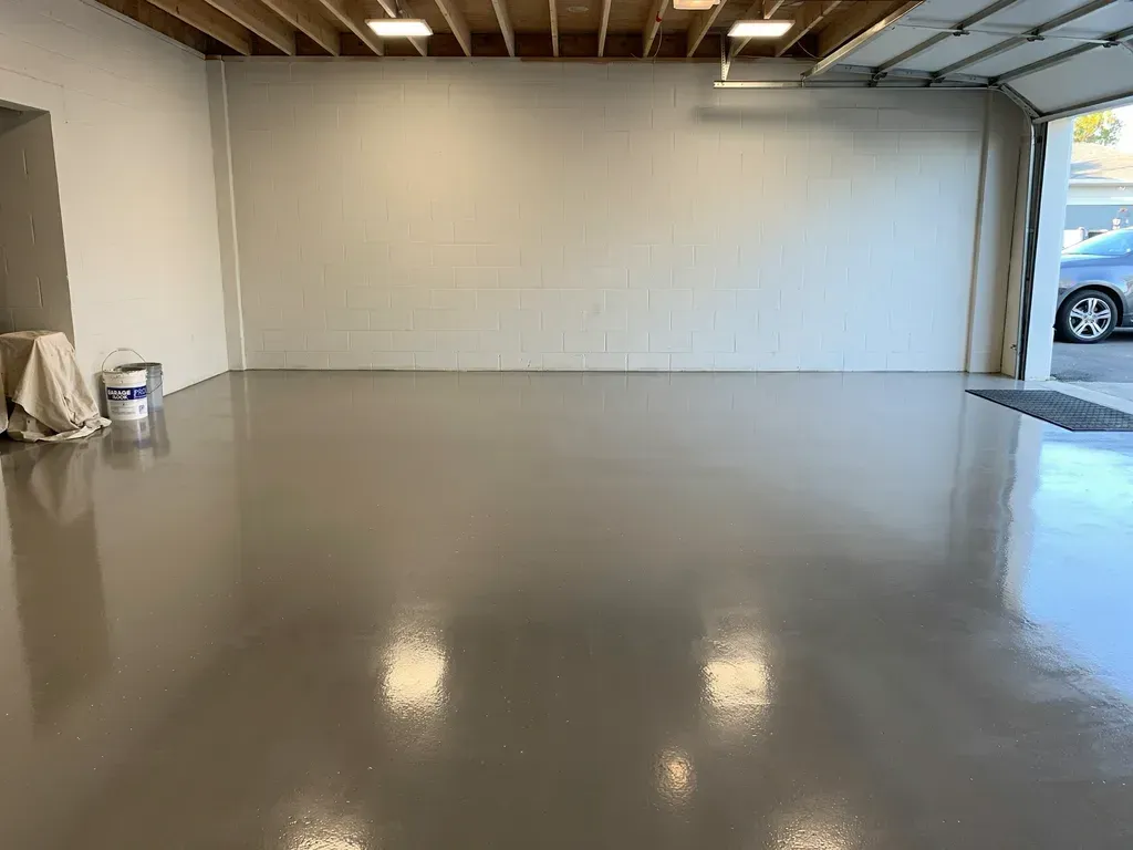 Empty garage with polished concrete floor and a white wall, lit by overhead lights.