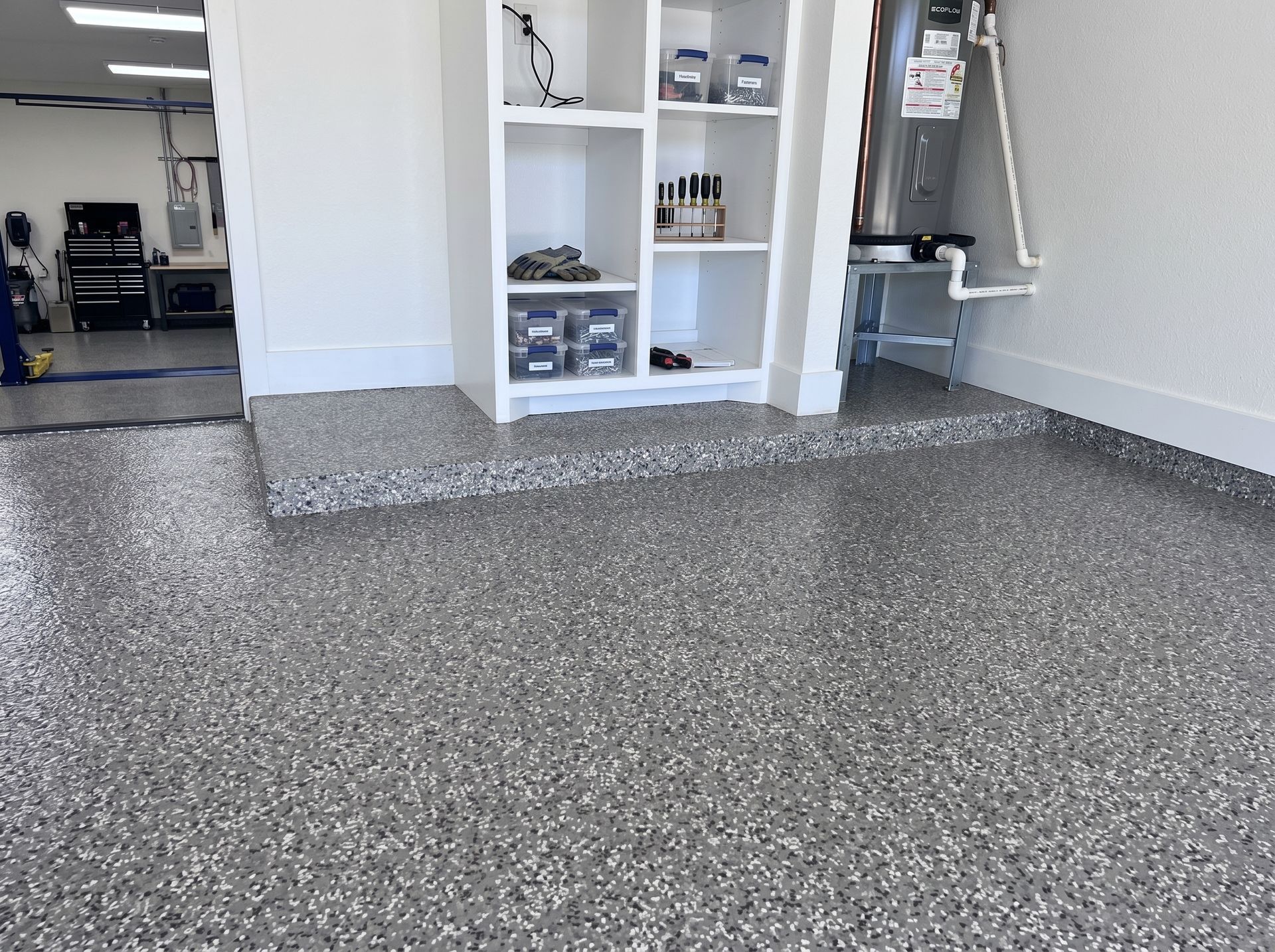Empty garage with glossy black floor, white walls, and tools on a pegboard near the open door.