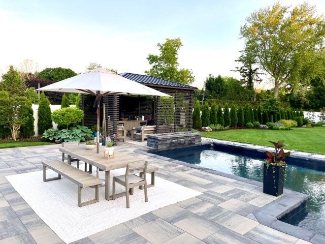 Modern backyard patio with pool, dining table, lounge chairs, and pergola in a landscaped garden