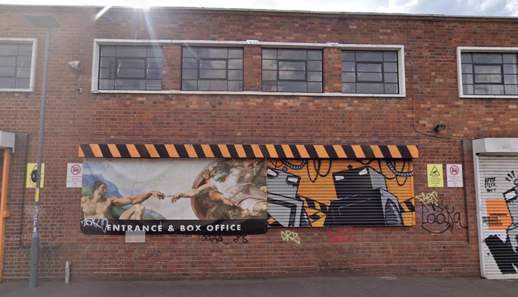 Brick building with mural of Michelangelo's Creation of Adam and graffiti art. Entrance/Box Office sign.