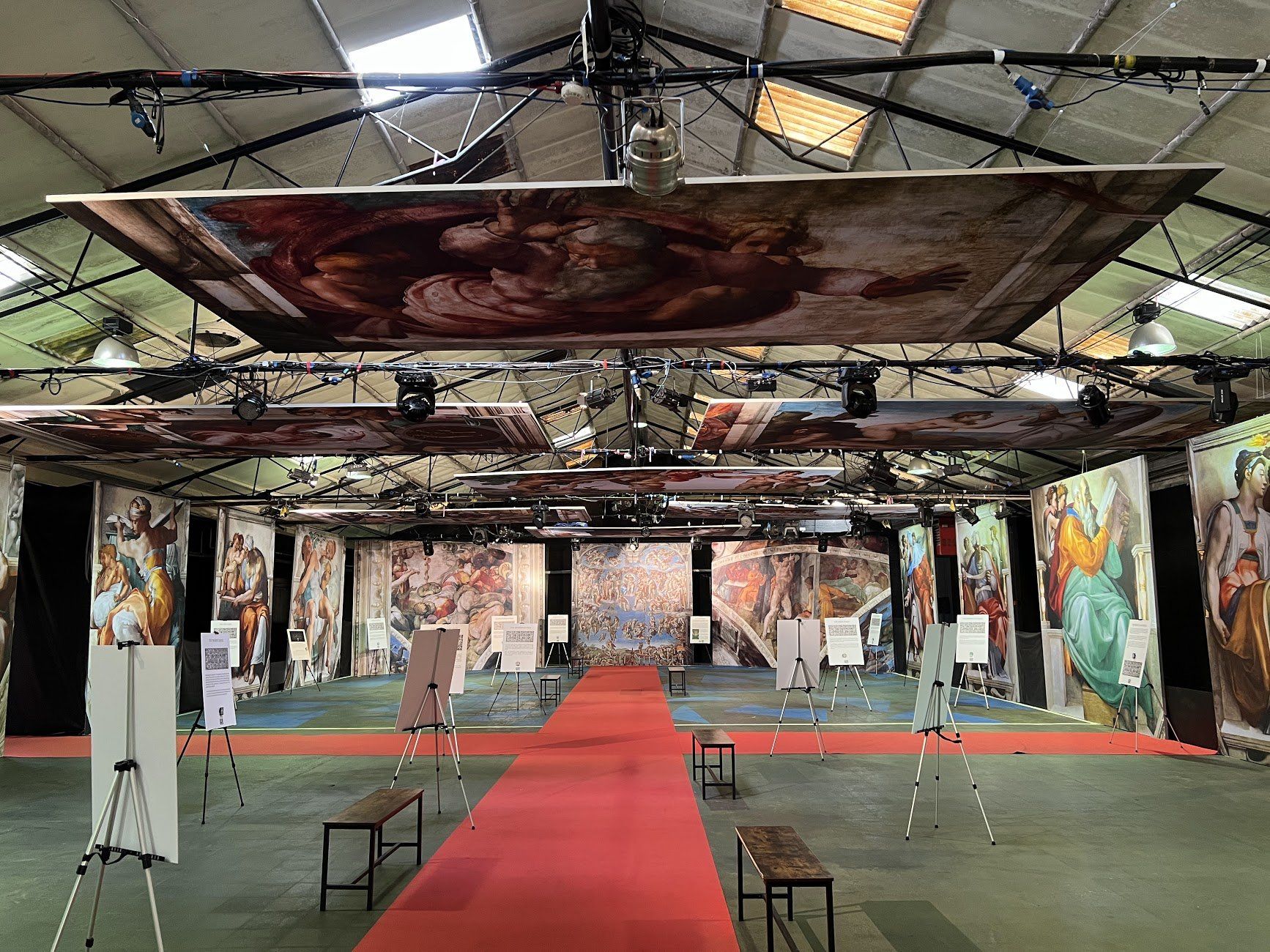Art gallery with paintings on walls and ceiling, red carpet.