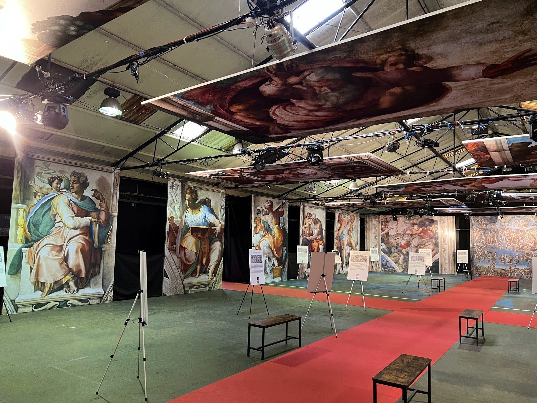 Exhibition hall with large reproductions of Renaissance art, including murals and figures, with a red carpet.