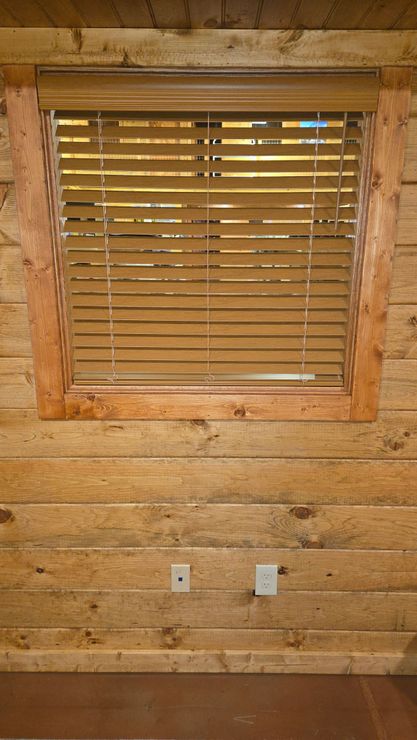 Wood-paneled wall with a small window covered by wooden blinds and two outlets below.