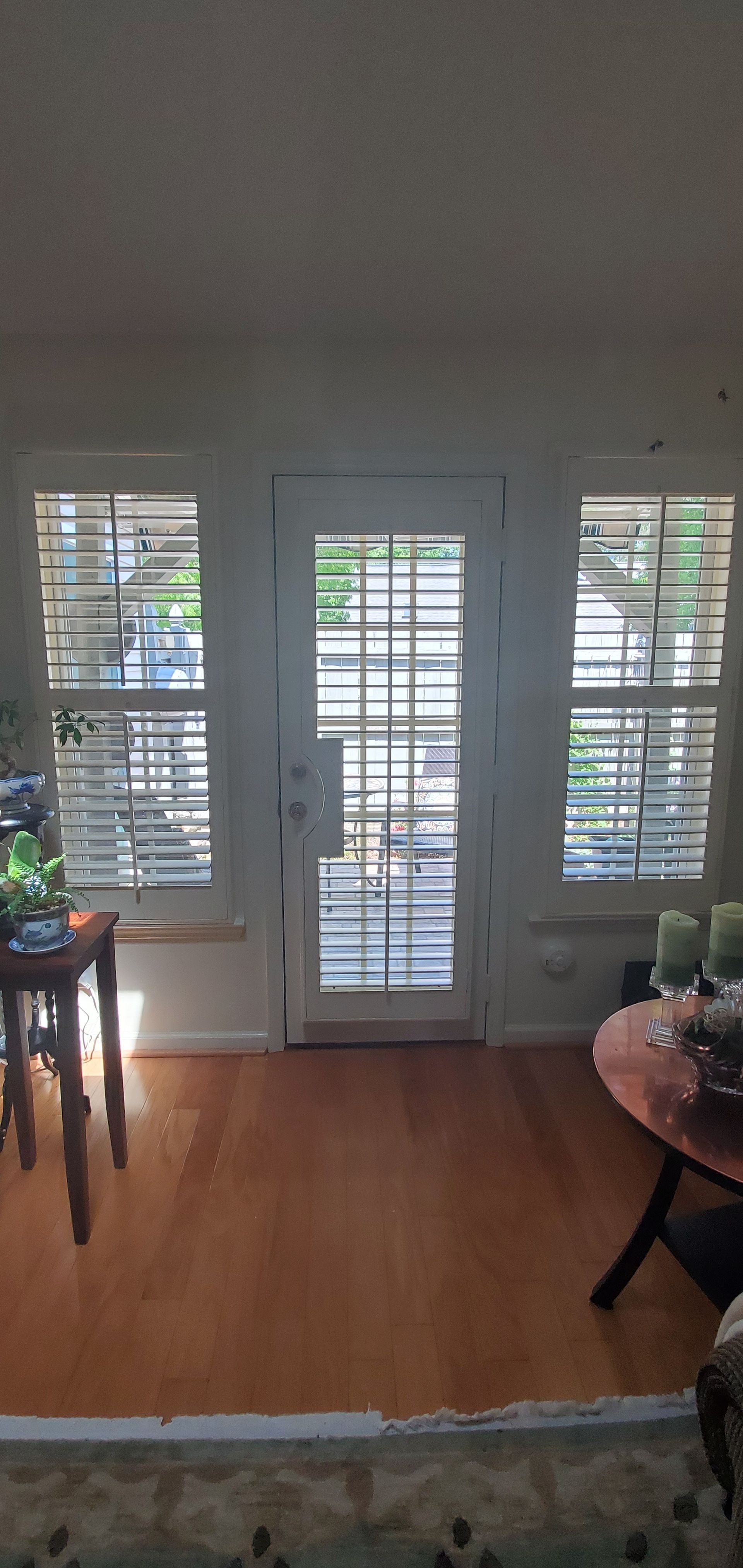 Bright room with French doors, white shutters, wood floor, and small tables on either side.