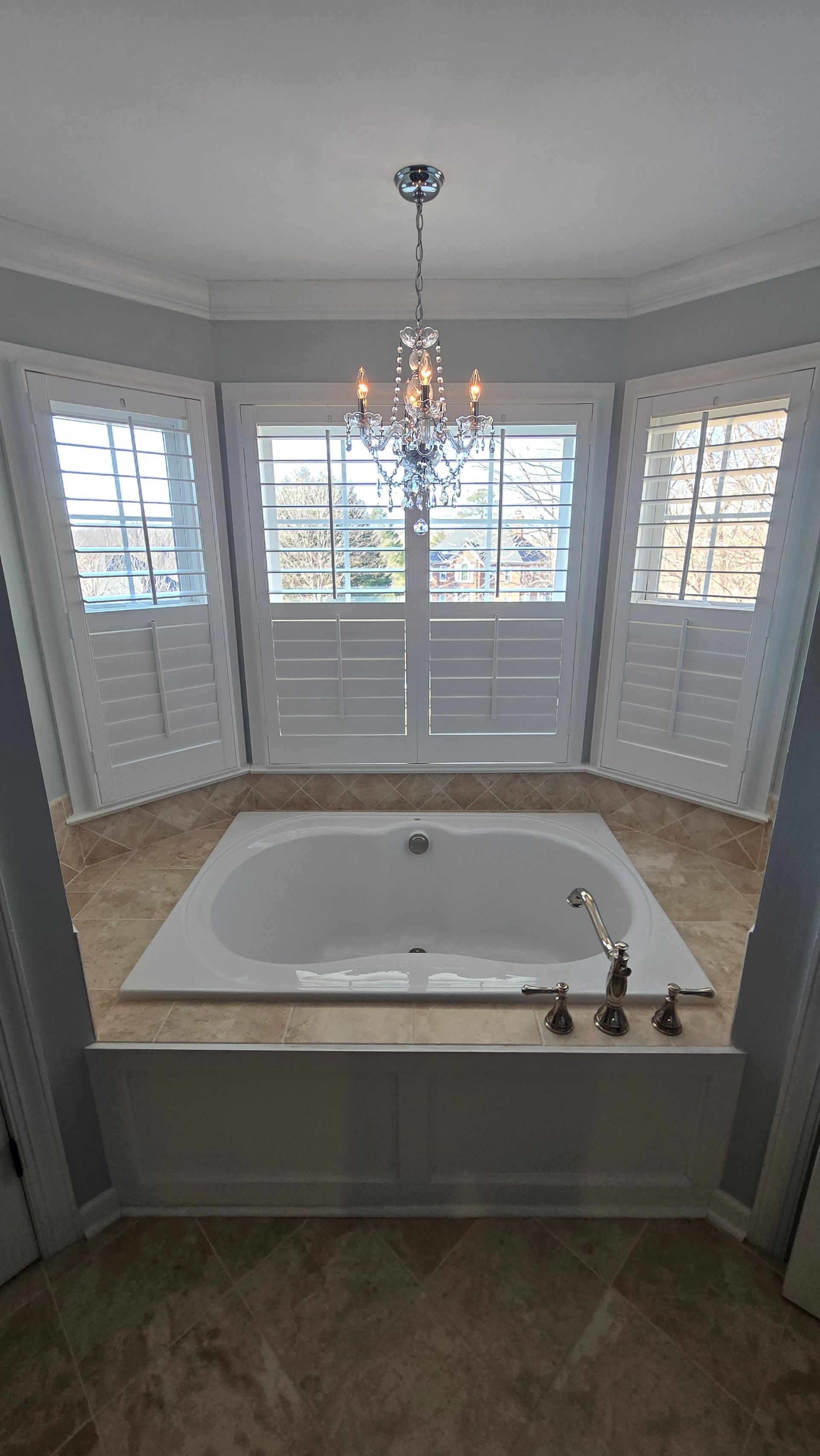 Bright bathroom with a white soaking tub, chandelier, bay windows, and light gray walls.