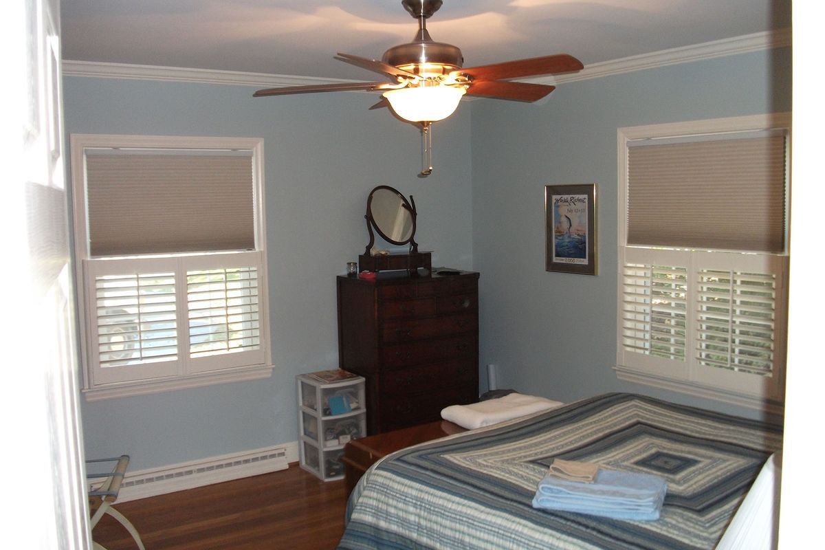 Bedroom with blue walls, two windows, a bed, dresser, ceiling fan, and wood floor.