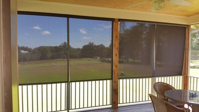 Covered patio with sliding glass doors overlooking a grassy field and trees