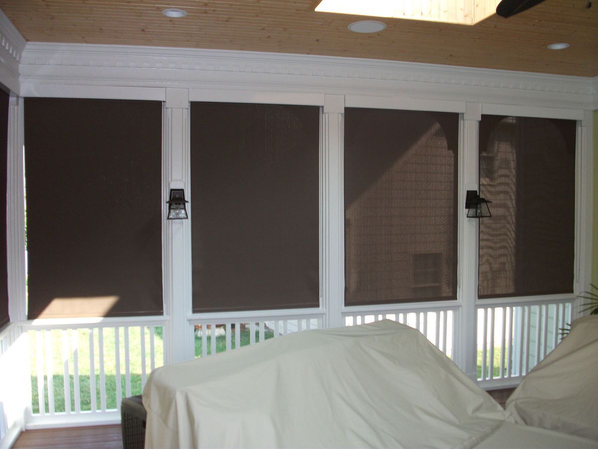Screened porch with dark shades over windows and furniture covered in white sheets