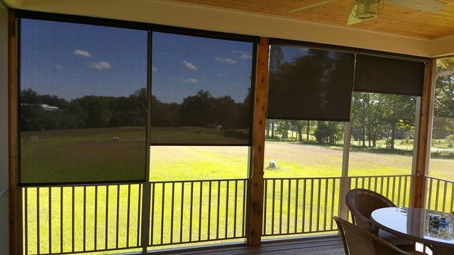 Screened porch overlooking a sunlit green lawn and trees, with a table and chairs at right