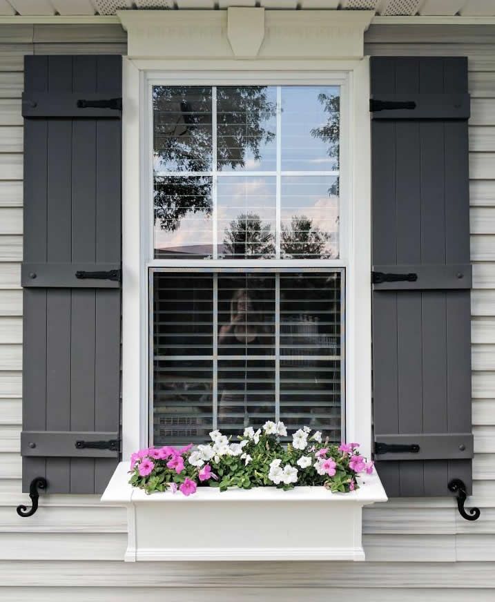 White window with dark shutters and flower box of pink and white flowers on a house exterior