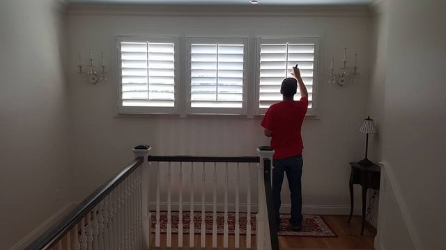 Person in a red shirt adjusting shutters in an upstairs hallway by a staircase.