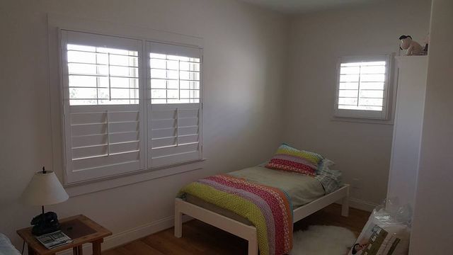 Small bedroom with a twin bed, colorful striped blanket, windows with shutters, and a bedside table lamp