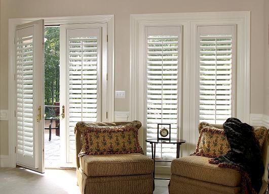 Bright living room with white shutters, wicker chairs, and an open door to greenery outside