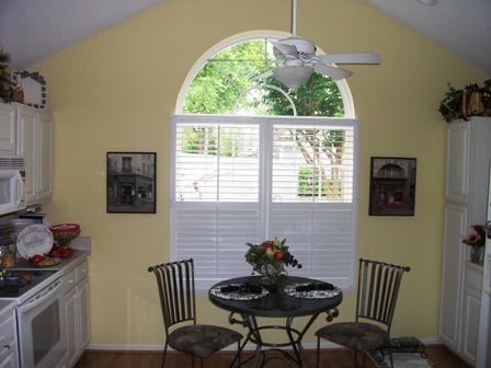 Small dining nook with round table, chairs, and a large arched window with white shutters.