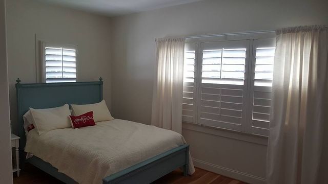 Bright bedroom with a teal bed, white bedding, and large window shutters with curtains