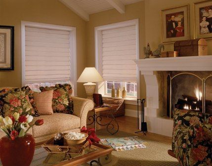 Cozy living room with floral sofa, armchair, fireplace, lamp, and window blinds
