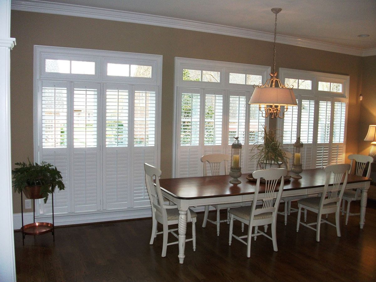 Dining room with white shutters, wooden table, white chairs, and a hanging light fixture
