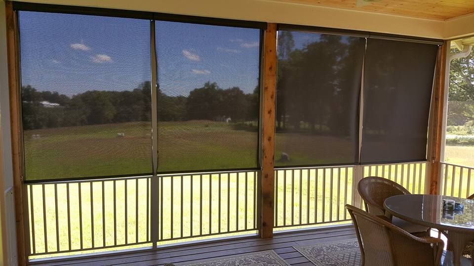 Enclosed porch with screened windows overlooking a green field, wood ceiling, and table with chairs.
