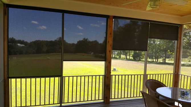 Covered porch with screened windows overlooking a green yard and trees, with a table and chair on the right.