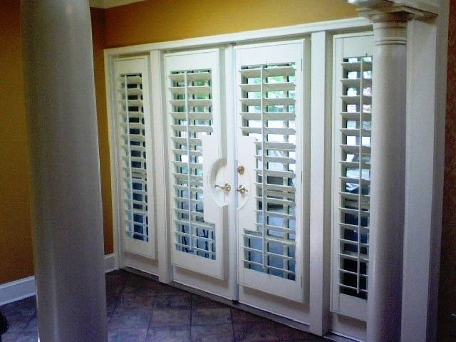 White plantation shutters on double French doors in a hallway with yellow walls and a column.