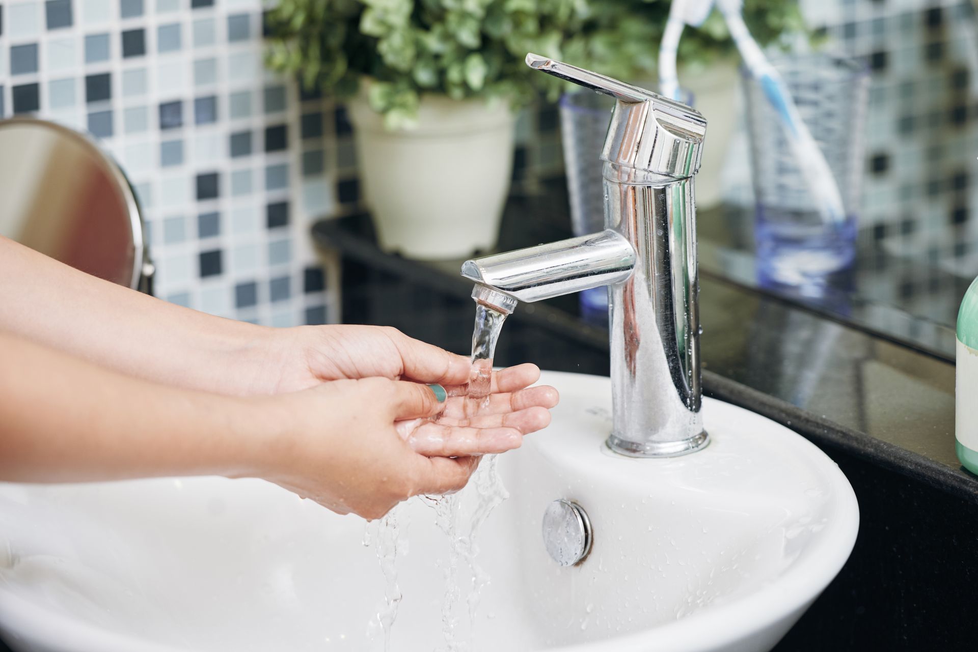 Hands being washed under running water at a bathroom sink with chrome faucet. Hands being washed under running water at a bathroom sink with chrome faucet.