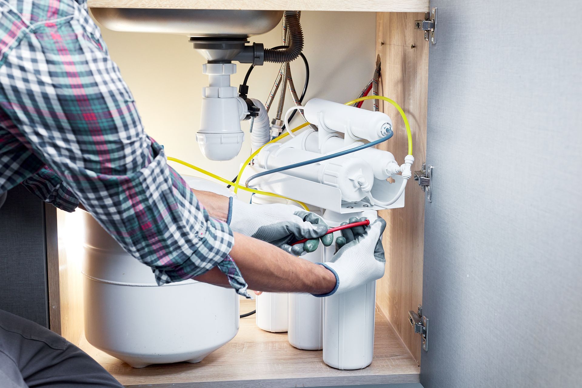 A technician installs a water filtration system on the PVC pipes of a sink.