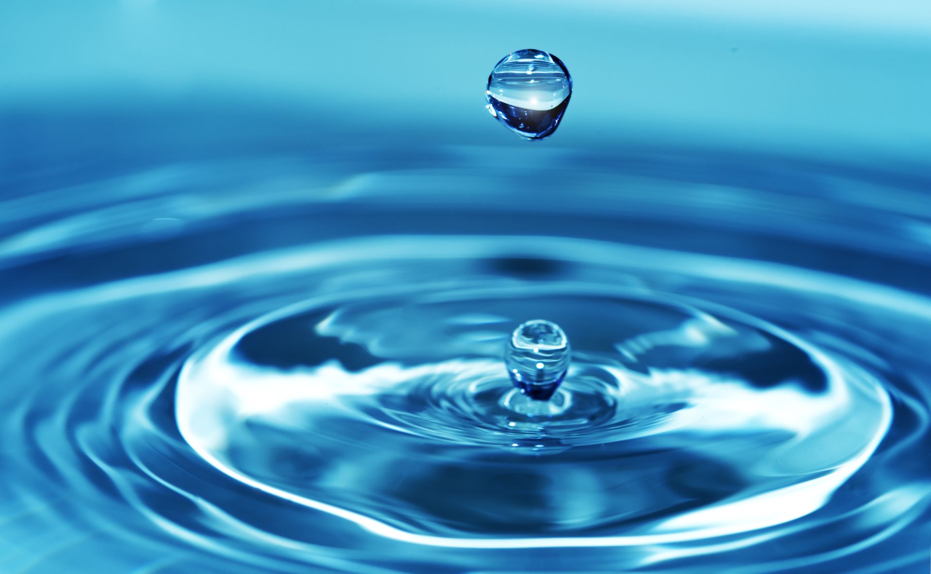 A single water droplet splashing into blue water, creating circular ripples. A single water droplet splashing into blue water, creating circular ripples.