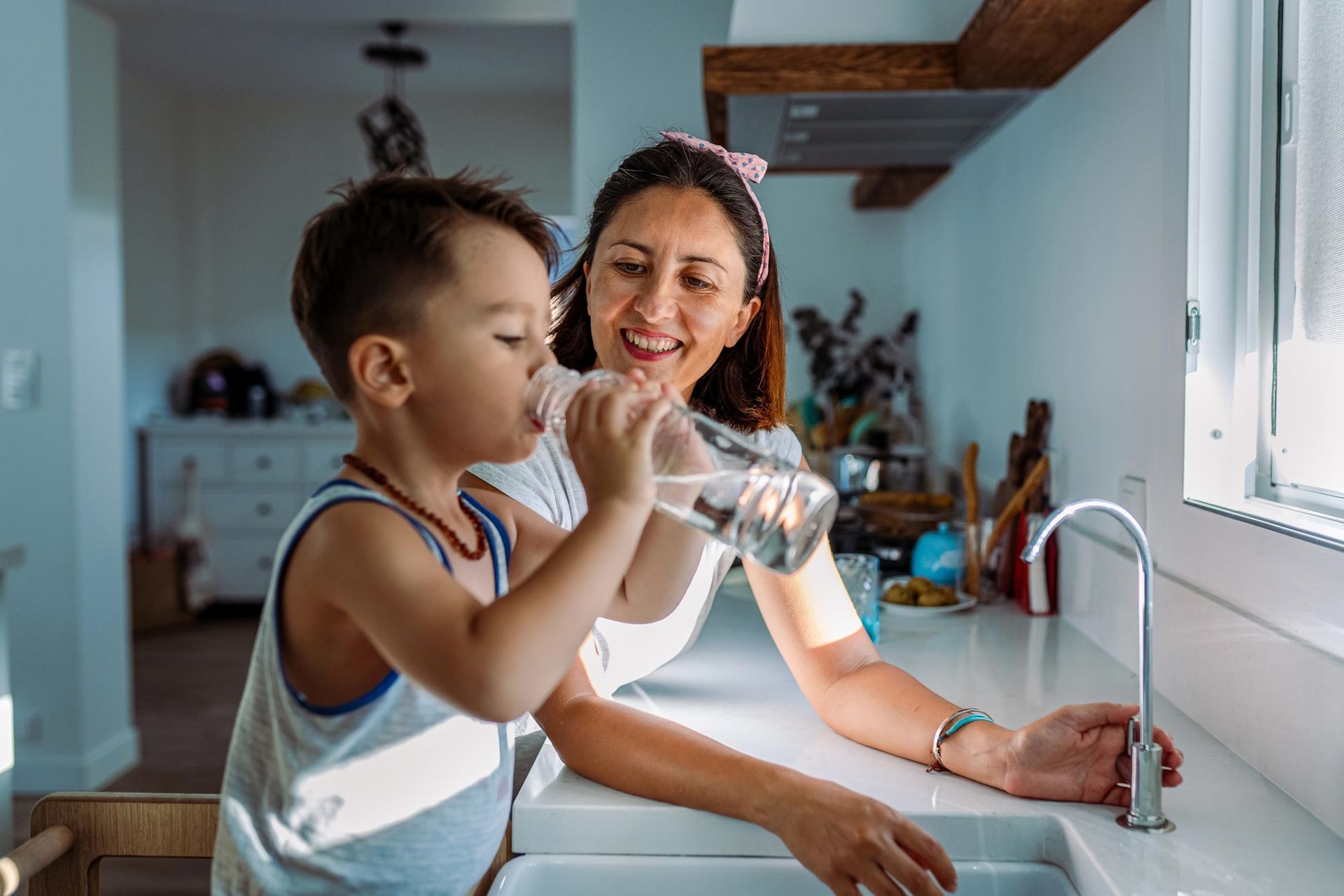 Mother and toddler filling a glass with water from a home water conditioning system by Olympic Sprin