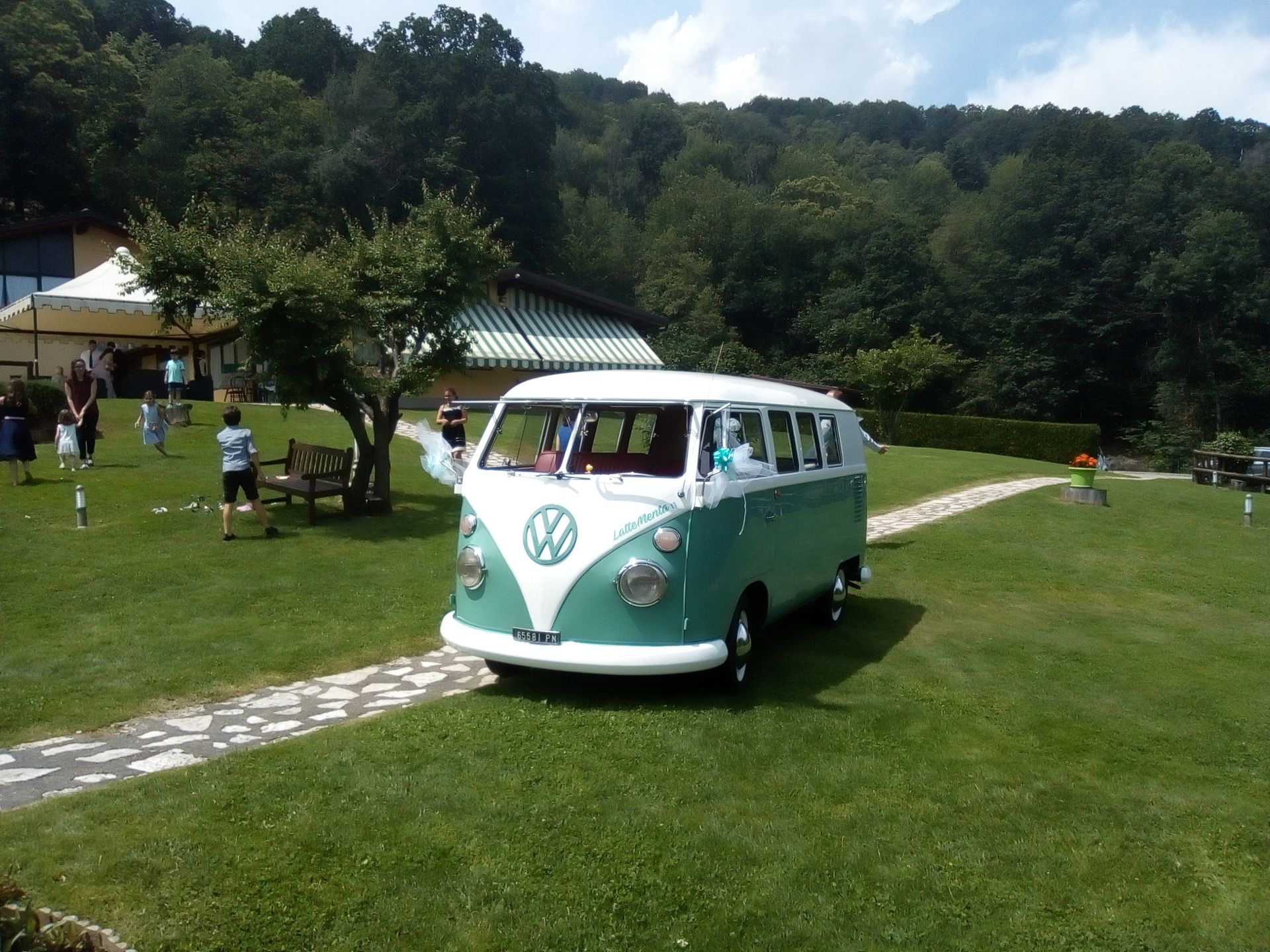 Un pulmino Volkswagen verde acqua e bianco su un prato erboso con alberi sullo sfondo.