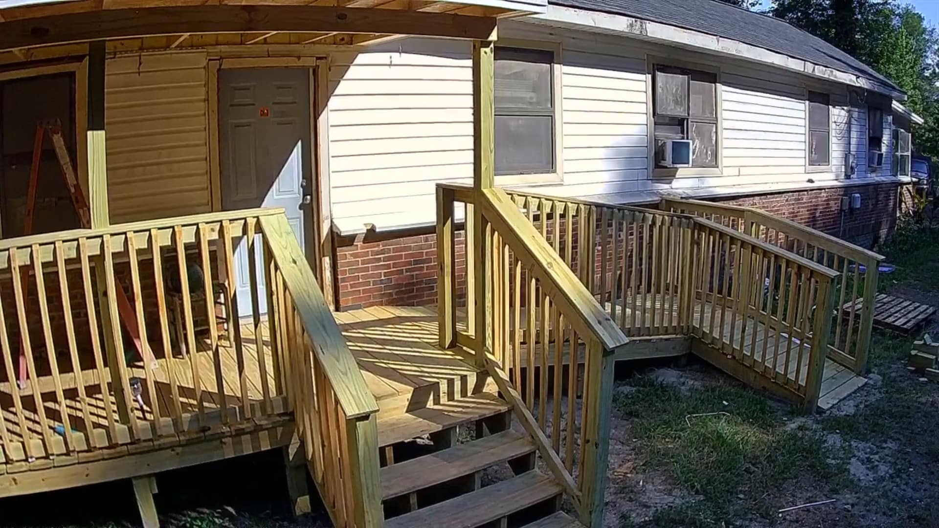 Wooden deck with stairs leading up to a house with beige siding, a door, and windows.