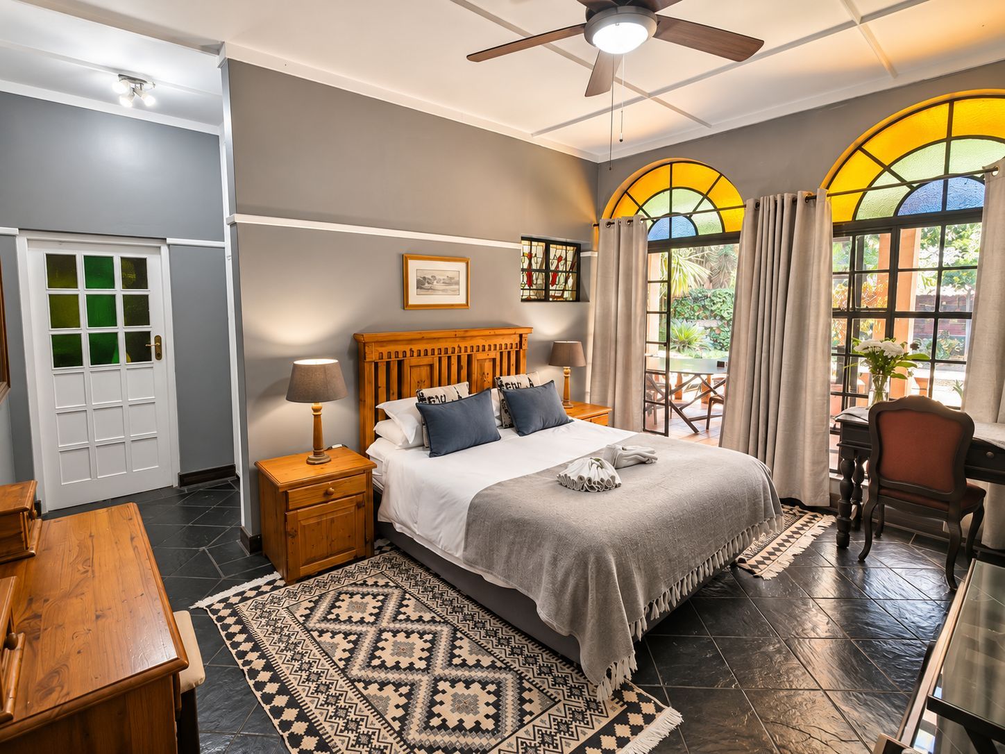 Cozy bedroom with wooden bed, gray walls, patterned rug, and arched windows letting in warm daylight