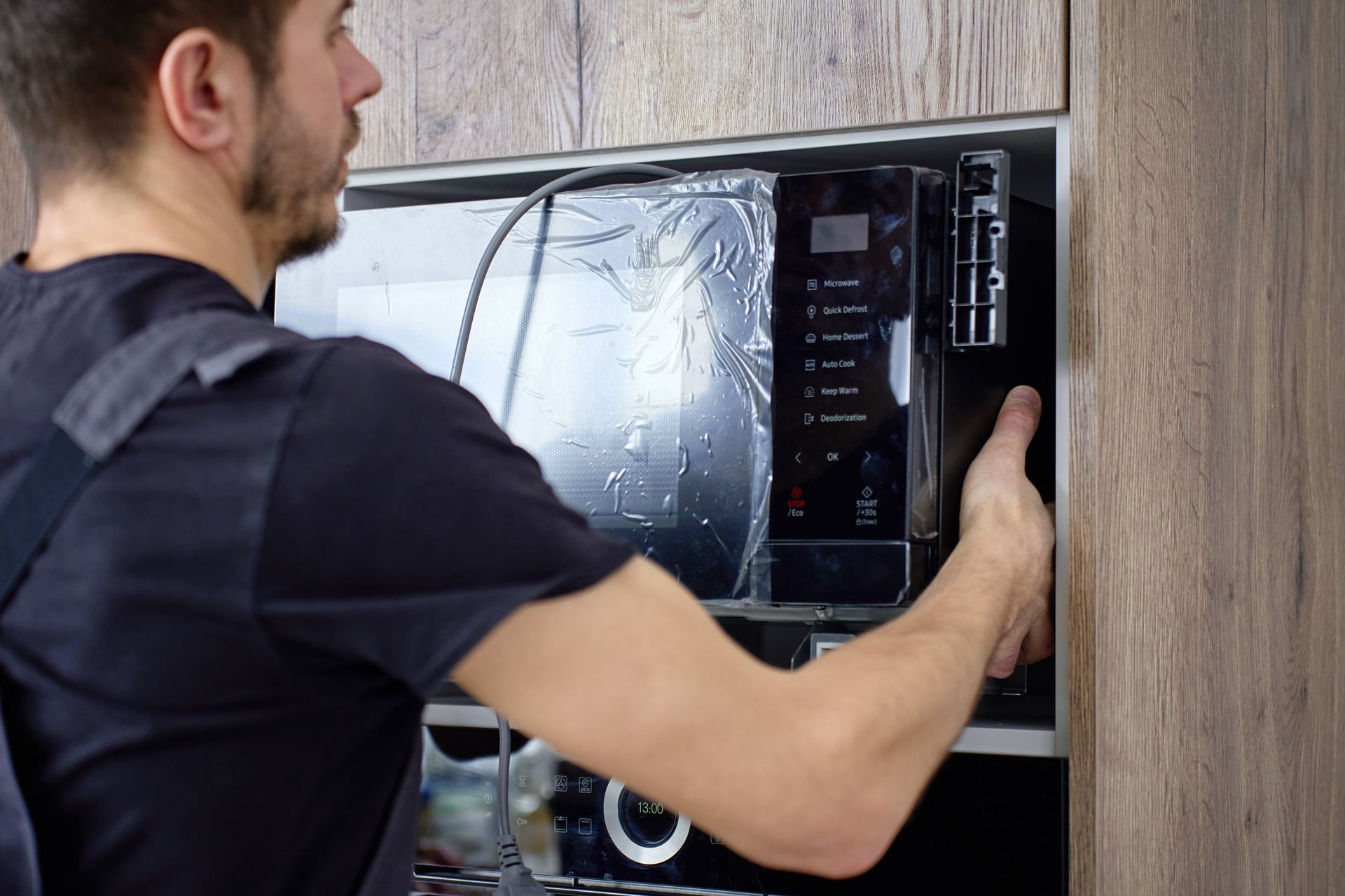 Man installing a microwave oven into a wooden kitchen cabinet, holding the door open