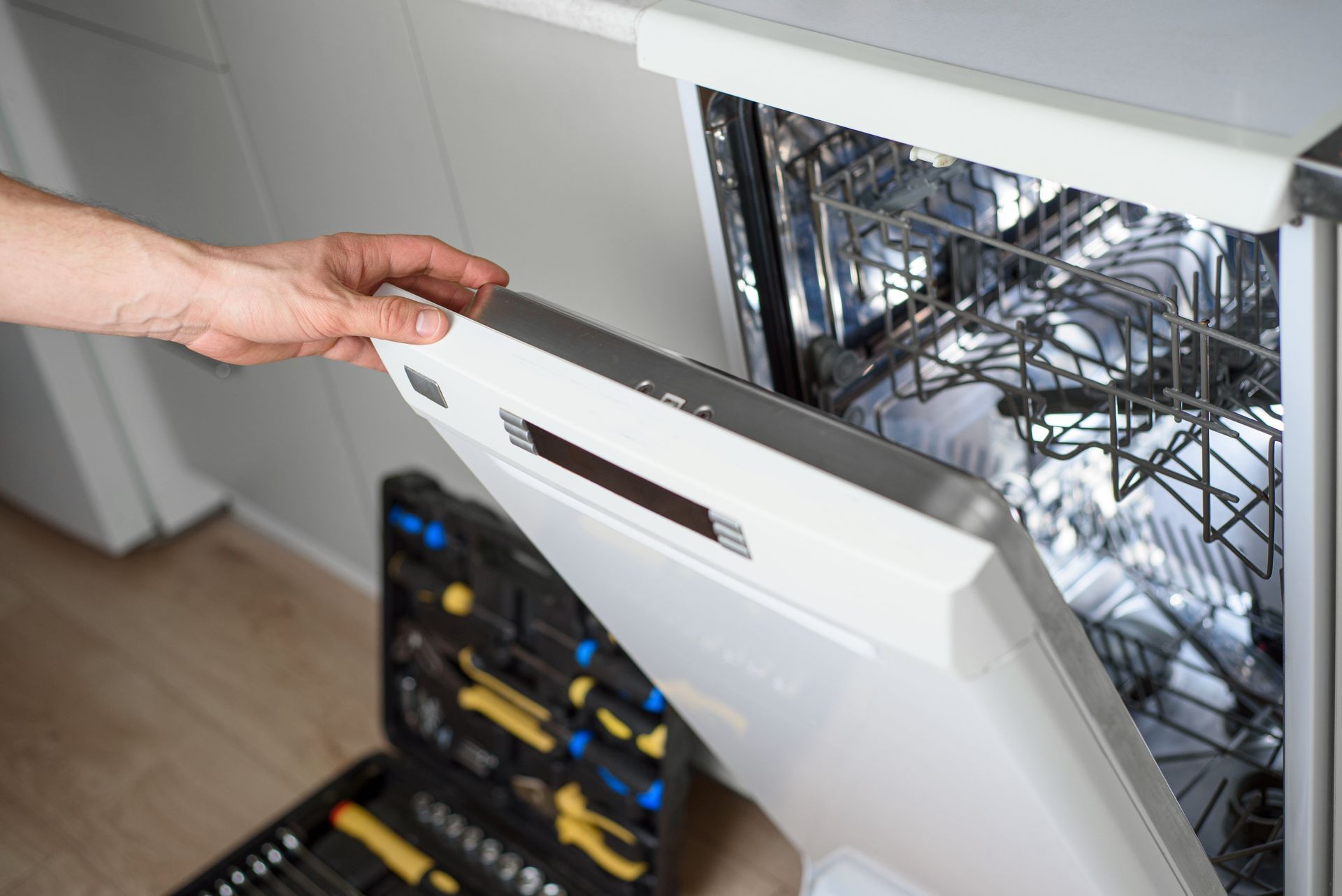 Hand opening a dishwasher door in a kitchen, with racks visible inside