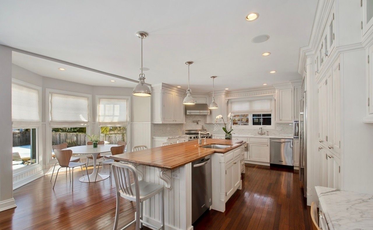 A kitchen with white cabinets and hardwood floors and a large island in the middle.