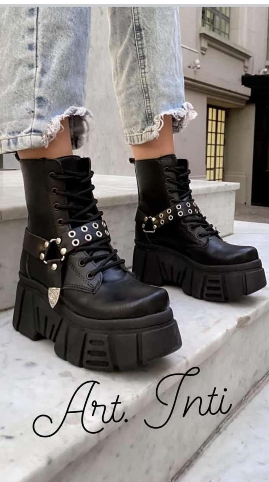 Botas negras de plataforma gruesas con correas con tachuelas sobre vaqueros desgastados de lavado claro en las escaleras