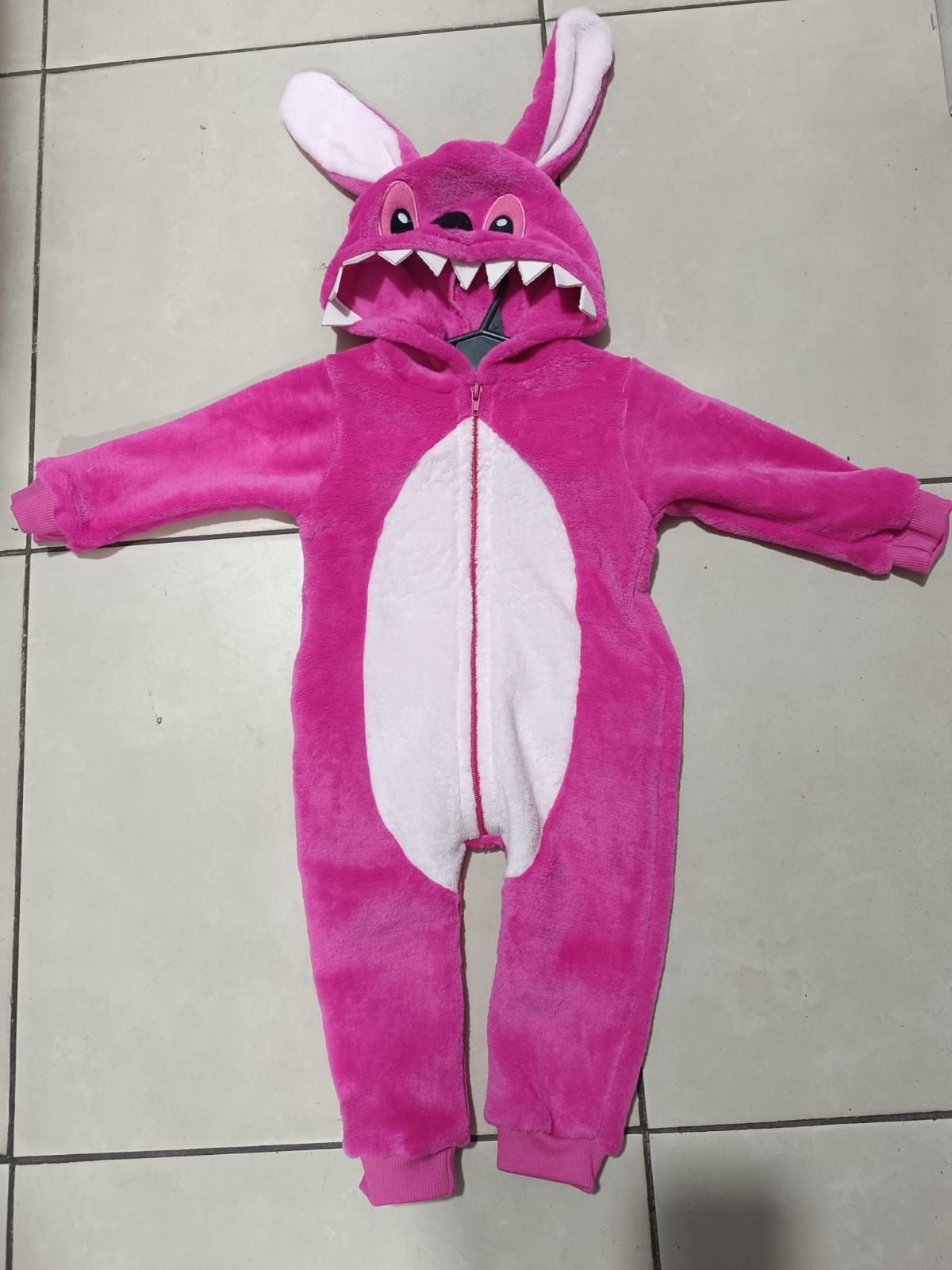 Disfraz de conejito rosa con barriga y orejas blancas, extendido sobre un suelo de baldosas.