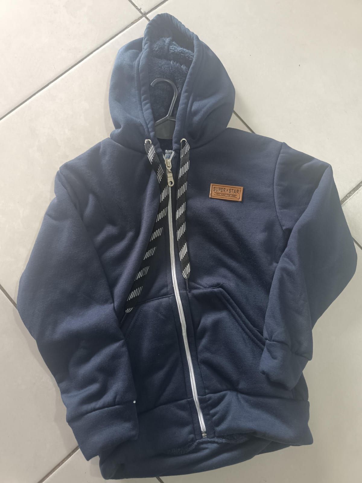 Sudadera con capucha y cremallera de color azul marino, extendida sobre un suelo de baldosas claras.