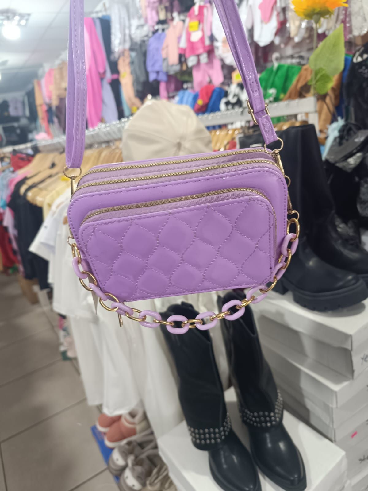 Bolso bandolera acolchado morado con correa de cadena dorada colgado en una tienda de ropa.