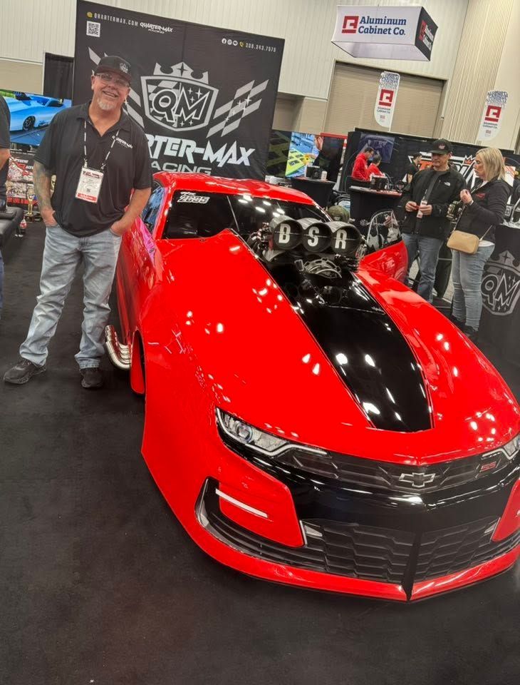 Red sports car on display at an auto show, with two people standing beside it.