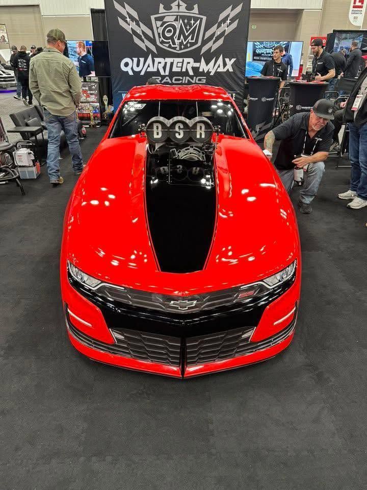 Red custom race car with black hood cutout on display at an auto show booth.
